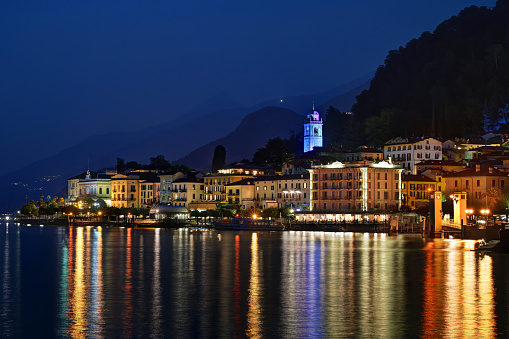 Scenic view of town of Bellagio at Como Lake with buildings and mountains in background against blue twilight sky during summer in Italy, Europe