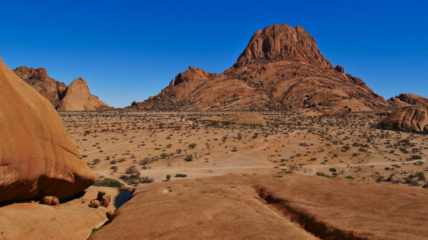 istock Panoramic view over mountain Spitzkoppe, Kalahari desert, Namibia, with little water pond and round shaped brownish rocks. 1276609931