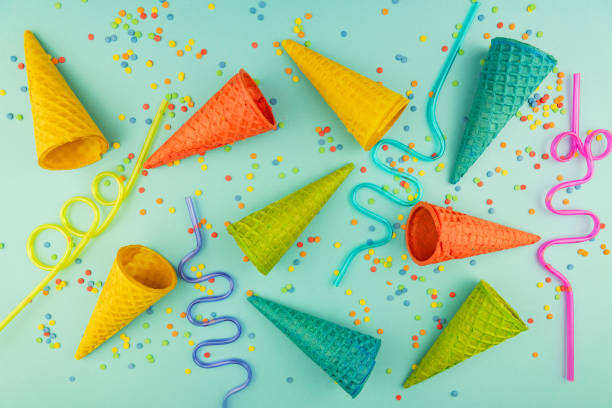 istock bright multicolored ice-cream waffle cones and cocktail straws on blue background with scattered confetti sugar sprinkles. 1276610154