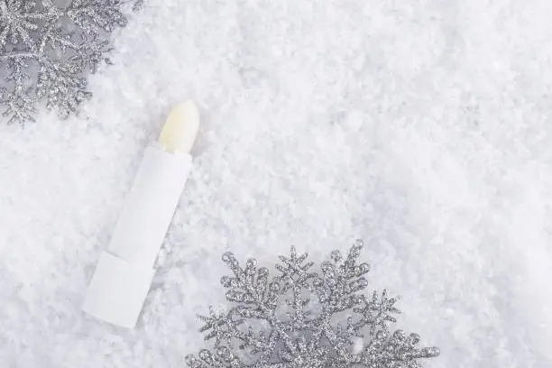 Photo of A tube of colorless lipstick balm to protect and nourish lips. Winter season cosmetics. Mock up container near with snowflakes, in the snow. Christmas present for women idea. Banner. Copy space