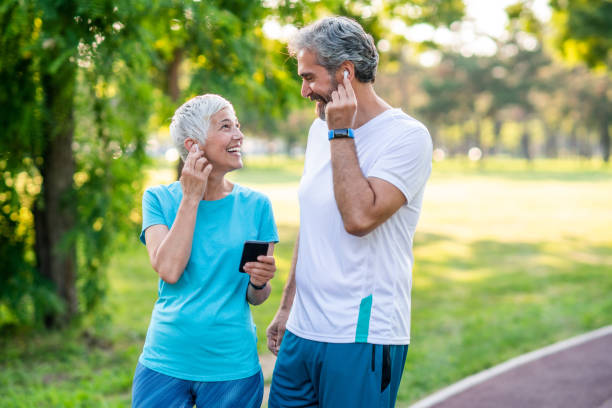 Smiling mature couple in sports wear jogging together. Using smartphone and touching their in-ear headphones.