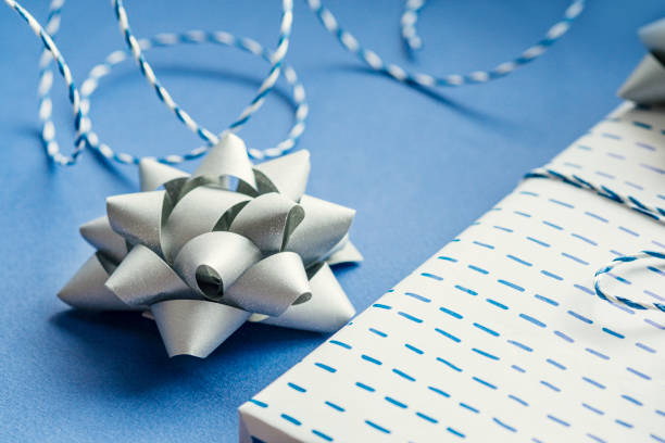istock Gift packaging: silver bows for gift decoration, blue gift rope, gift in a white box on a blue background. Preparing for Christmas holidays. Selective focus 1276616502