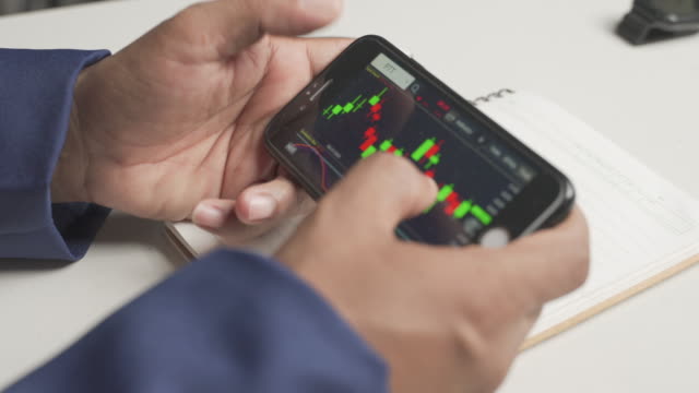 close-up of a man's hand trading stocks through a smartphone.