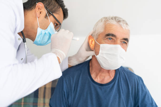 le travailleur de la santé examine l’oreille de l’homme aîné dans sa maison - scrubs professional sport indoors healthcare and medicine photos et images de collection