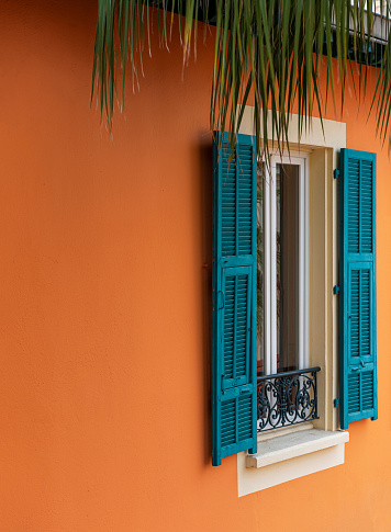 Vibrant color single window and blinds on orange color wall in Nice city, France.