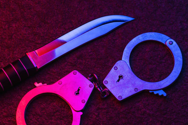 Handcuffs and a knife on a stone surface illuminated by the flashing lights of a police car. Concept on the topic of punishment for a committed crime Handcuffs and a knife on a stone surface illuminated by the flashing lights of a police car. Concept on the topic of punishment for a committed crime knife crime photos stock pictures, royalty-free photos & images