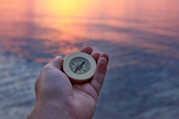 mano del hombre con una brújula en la costa del mar al amanecer. - compass exploration the way forward beach fotografías e imágenes de stock