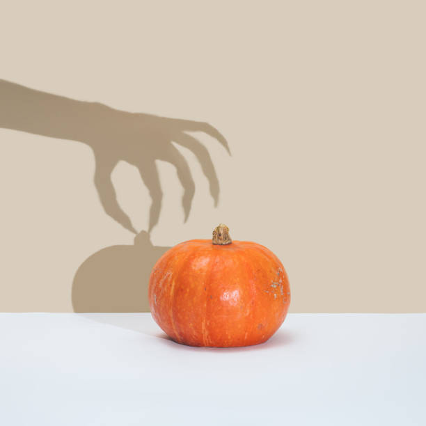 Halloween minimal concept with pumpkin and witch or zombie hand shadow.