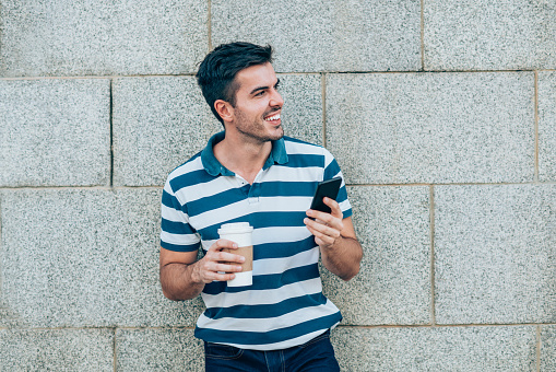 Young man texting on smart phone and holding coffee cup in the city.