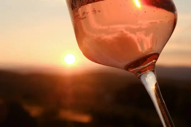 A glass of „Rose Sparkling Wine“ (Frizzante) against the sunset. Clouds are reflected in the glass.