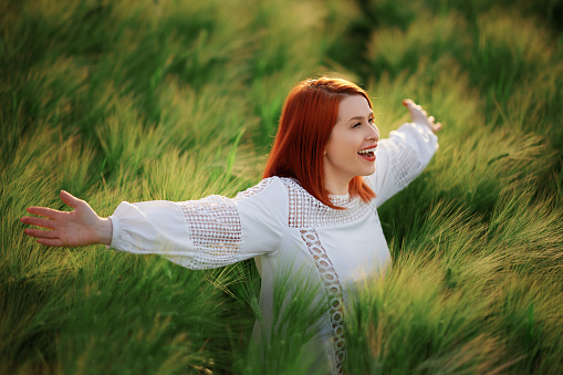 Redhead feeling freedom in the green meadow looking up admiring view
