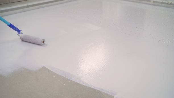 istock Concrete Floor repair work. Paint roller in construction site. A worker paints the concrete floor with a roller white. 1276631427