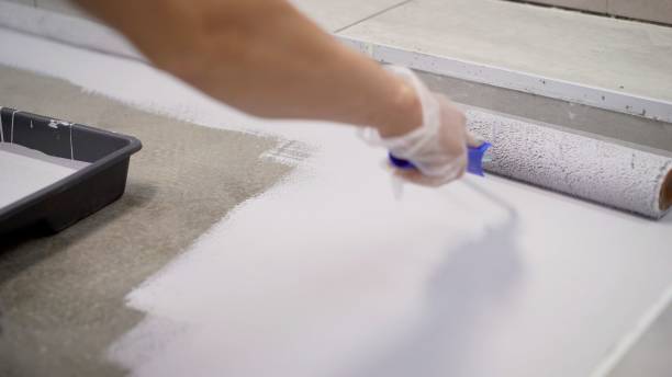 istock Concrete Floor repair work. Paint roller in construction site. A worker paints the concrete floor with a roller white. 1276631460