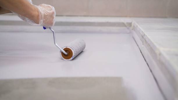 istock Concrete Floor repair work. Paint roller in construction site. A worker paints the concrete floor with a roller white. 1276631491