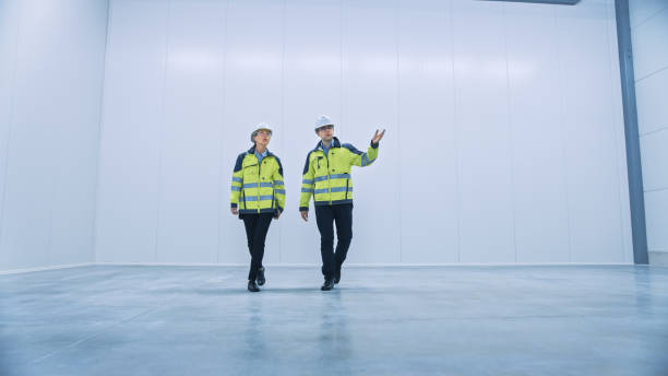 istock Two Engineers Talking, Walking Across Empty Factory Floor, Inspecting, Planning Where All the Machinery Would go. Professionals Industrial Designers Strategizing about New Manufacturing Plant Design 1276633059