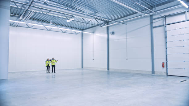 istock Industry 4.0 Modern Factory: Two Engineers in Empty Warehouse Use Digital Tablet Computer with Augmented Reality Software Visualizing of Manufacturing Plant Room Mapping. Illustrative Mock-up Concept 1276633093