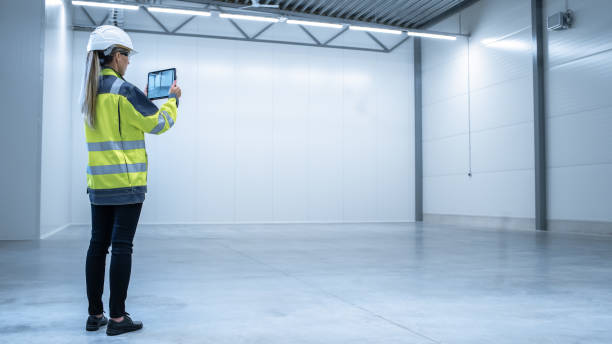 istock Industry 4.0 Modern Factory: Female Engineer is Stanging in Empty Warehouse and Using Digital Tablet Computer with Augmented Reality Software for Mapping Manufacturing Plant Room, Factory Layout. 1276633101