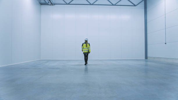istock Female Engineer Wearing Safety Hat Walks Across Empty Factory Floor, Inspecting, Planning Future Factory Layout. Professional Industrial Designer Strategizing about New Manufacturing Plant Design 1276633111