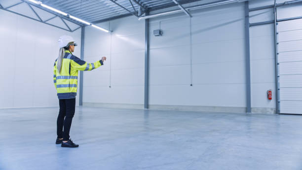 istock Industry 4.0 Modern Factory: Female Engineer Wearing Augmented Reality Headset Uses Mixed Reality Software and Gestures for Mapping Manufacturing Plant Floor for Future Machinery, Factory Floor Layout 1276633173