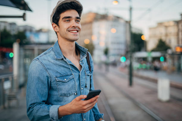 istock Handsome man using smart phone while waiting for a tram at the public transport stop 1276637827