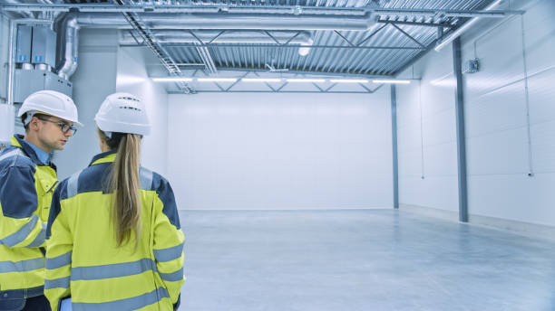 istock Two Engineers Talking, Standing in the Middle of an Empty Warehouse, Inspecting, Planning Future Factory Layout. Professionals Industrial Designers Strategizing about New Manufacturing Plant Design. 1276638148