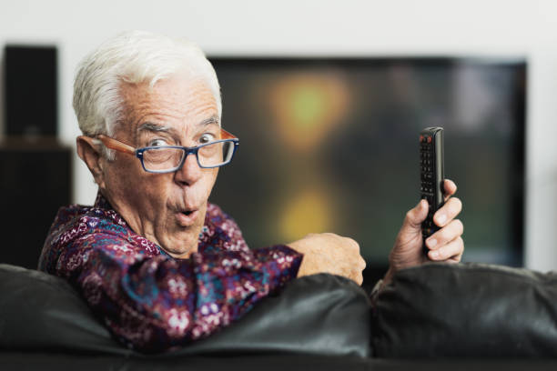istock Surprised or shocked senior man holding remote control in front of flat screen TV set 1276641583