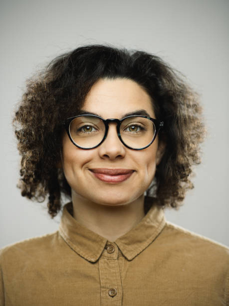 Studio portrait of young woman with happy expression Close-up portrait of young caucasian woman with happy expression against white gray background. Vertical shot of hispanic real people smiling with long curly hair and green eyes. Photography from a DSLR camera. Sharp focus on eyes. smirking stock pictures, royalty-free photos & images