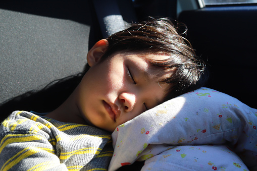 Portrait of sleeping little Asian boy on back seat of a car, exhausted after returning from a vacation outing.