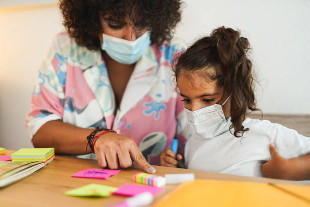 Mother doing home schooling with child while wearing surgical face mask for coronavirus Mother doing home schooling with child while wearing surgical face mask for coronavirus reopening photos stock pictures, royalty-free photos & images