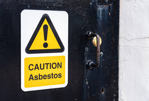 A sign on the entrance door to an old building, warning people of the health and safety dangers of asbestos being present.