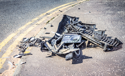 Bumpers, a front headlight cluster and other materials from a car discarded on a road following a crash.