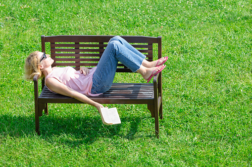 A woman is sunbathing on a Park bench with a book set aside