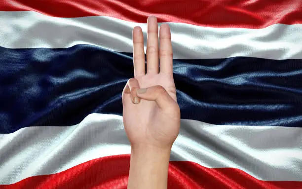 Photo of a hand showing 3 fingers, a political symbol, on Thai flag background