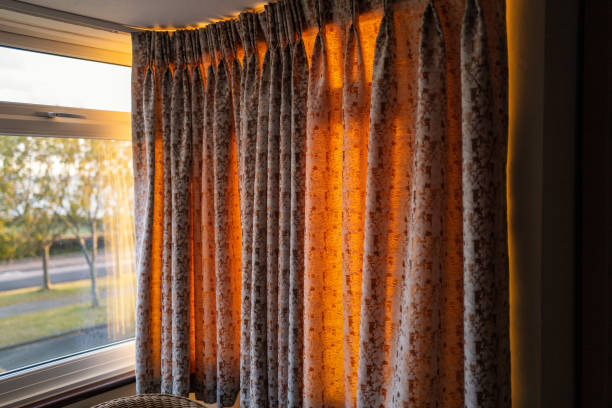 Golden light of a sunset glowing through hanging curtains on one side of a bay window Golden light of a sunset glowing through hanging curtains on one side of a bay window curtain rail stock pictures, royalty-free photos & images