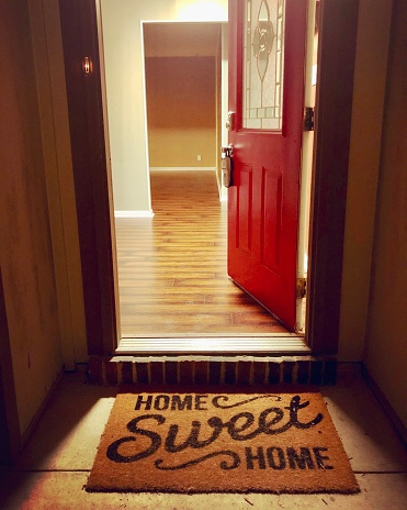 Rojo abierto puerta principal a una casa con un hogar dulce hogar alfombra de bienvenida photo