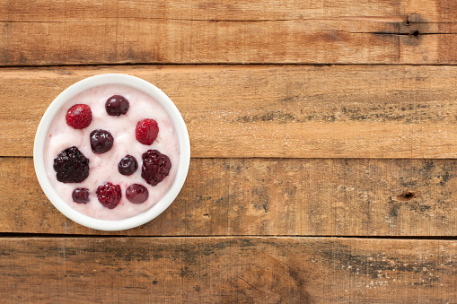 Top view of white bowl full of yogurt with berries over wooden table