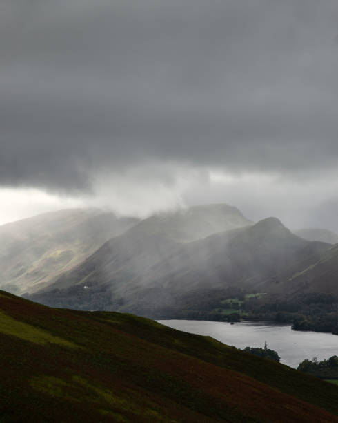 Beautiful landscape image across Derwentwater valley with falling rain drifting across the mountains onto the lush green countryside below