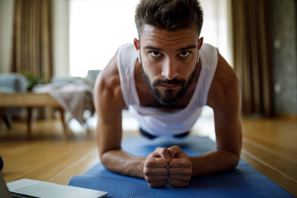 istock Young man with headphones using laptop for exercising at home 1276685908