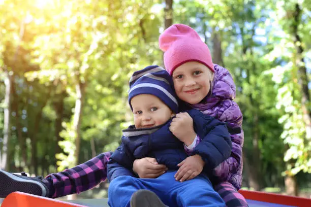 Two cute adorable playful caucasian siblings boy girl child enjoy havefun on playground at backyard or city park outdoors. Little toddler brother and sister portrait hugging and smiling. Family care.