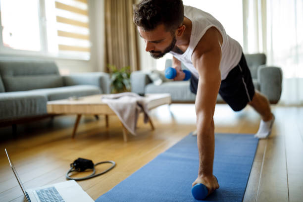 istock Young man using laptop and exercising at home 1276686126