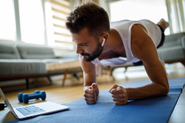 joven con auriculares usando portátil para hacer ejercicio en casa - body building exercises audio fotografías e imágenes de stock