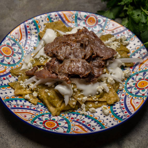 istock Mexican green chilaquiles with cecina beef steak on dark background 1276686214