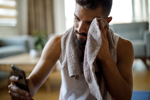 Young athletic man wiping sweat from forehead after exercise at home