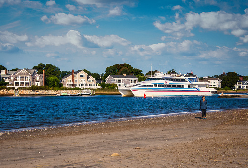 Yarmouth, Massachusetts, USA- September 23, 2020- A lone woman stands on the shore of Bay View Beach as she watches the high speed catamaran passenger ferry boat 