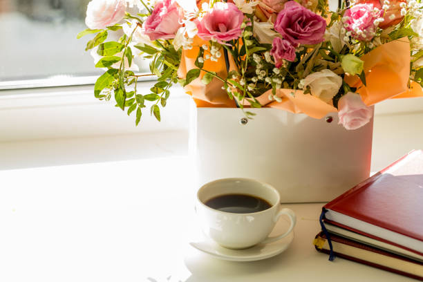 light romance background. coffee cup with notepad and flowers bouquet on a window sill. love and romance concept.