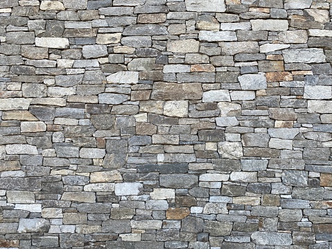 Wall of oddly shaped, grey and other earth-tone bricks made of rock, creating abstract background texture suitable for compositing