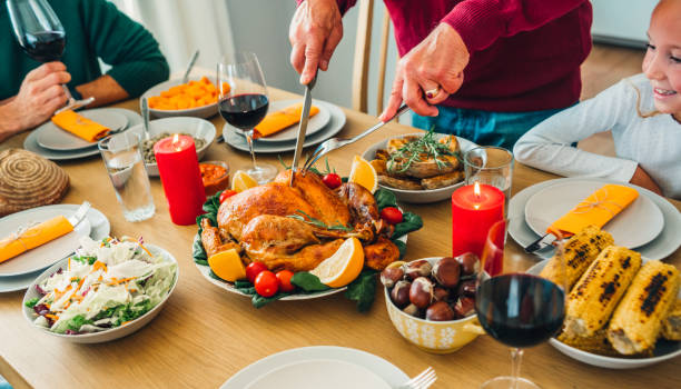 Unrecognizable person carving roasted turkey during holiday dinner at dining table.