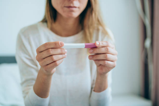 mujer joven triste con prueba de embarazo en casa - prueba de embarazo fotografías e imágenes de stock