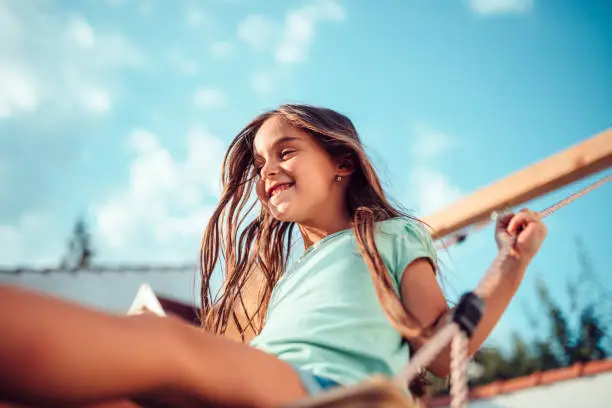 Portrait of a happy little girl wearing green shirt sitting on a swing and smiling