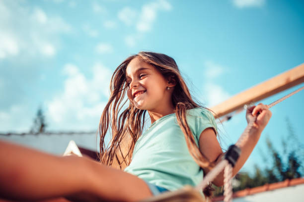 portrait of a happy little girl sitting on a swing and smiling - swinging imagens e fotografias de stock